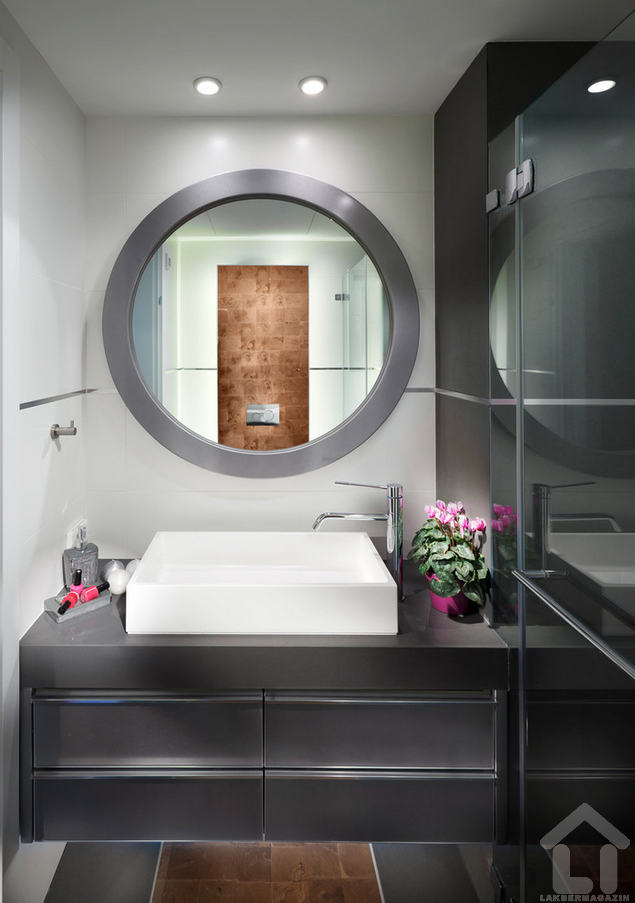 a kerek tükörrel itt kellemes kontrasztot ad a szögletes fehér mosdó, a bútor a falra erősítve szinte "lebeg", látványos extra világításra ad lehetőséget