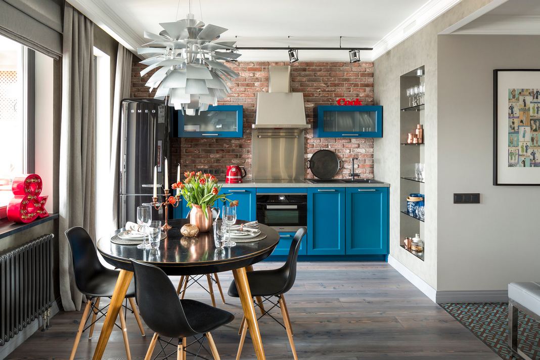 Az alábbi lakásban a tervező bátran nyúlt a színekhez és a stílusokhoz - pl. fekete retro hűtőszekrénnyel, kék konyhabútorral, tégla hátfallal, dizájn lámpával