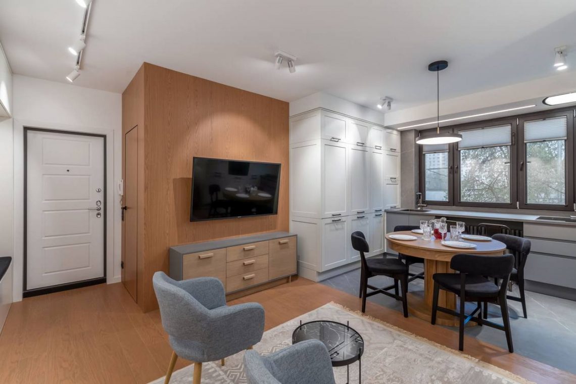 Egybenyitott nappali-konyha tér látványos és funkcionális berendezése fehér és fa felületekkel