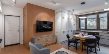 Egybenyitott nappali-konyha tér látványos és funkcionális berendezése fehér és fa felületekkel