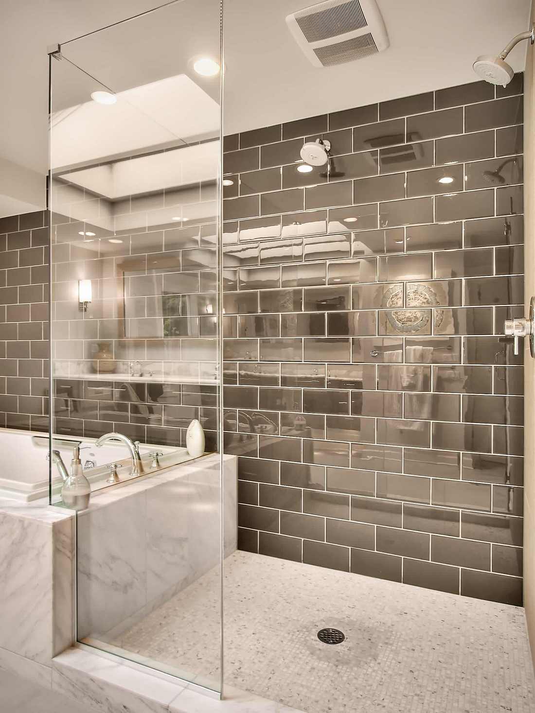 Modern fürdőszoba márvány fürdőkáddal, dupla üvegfalú zuhanyfülkével. A zuhanyfülke padlója mozaik, a fal kobaltszürke tükör metro csempével burkolt.