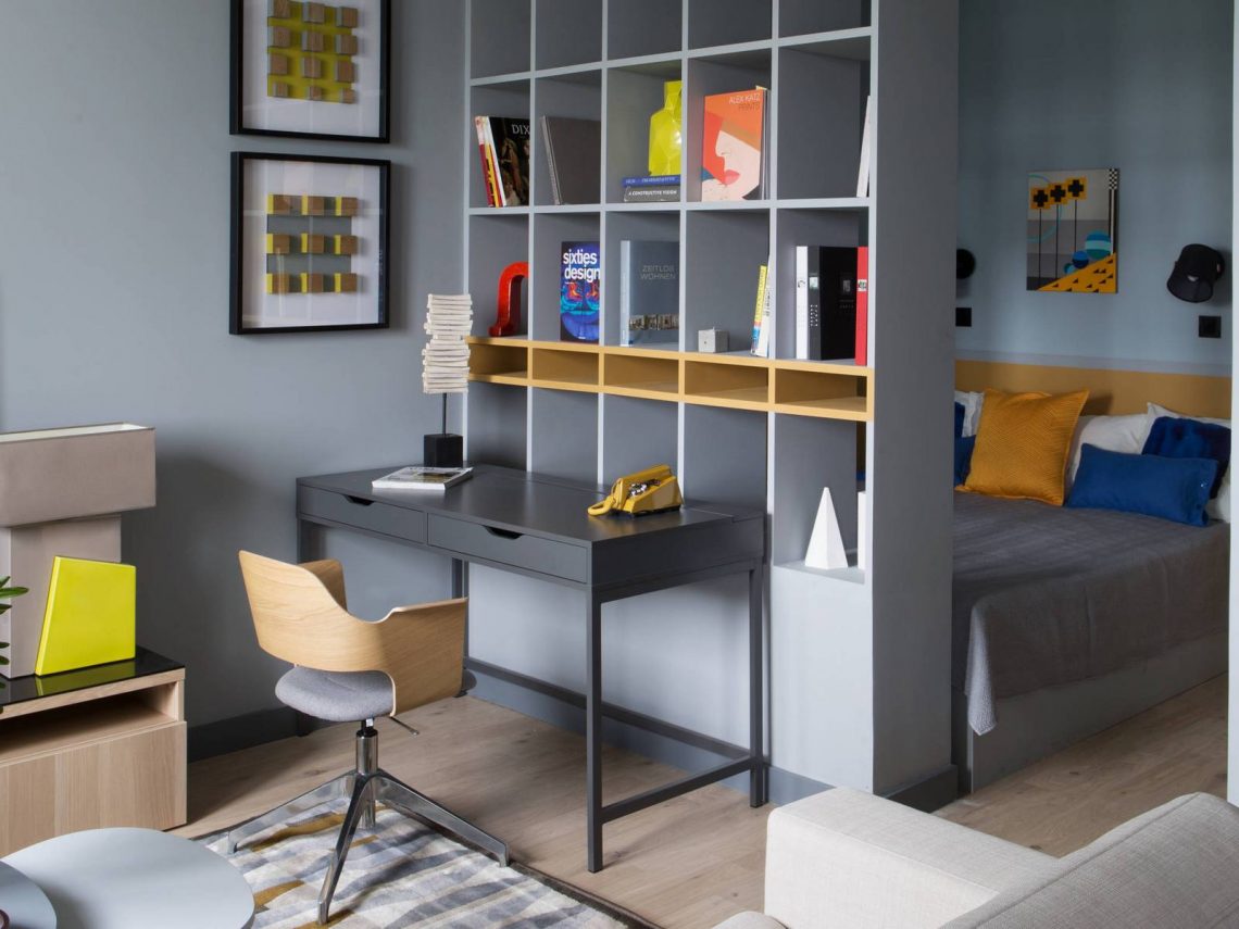 Fiatal pár egyszobás lakása egyszerű, praktikus, modern berendezéssel, 45m2 - szürke, sárga, kék színpaletta, polcos térelválasztó nappali és háló zóna között