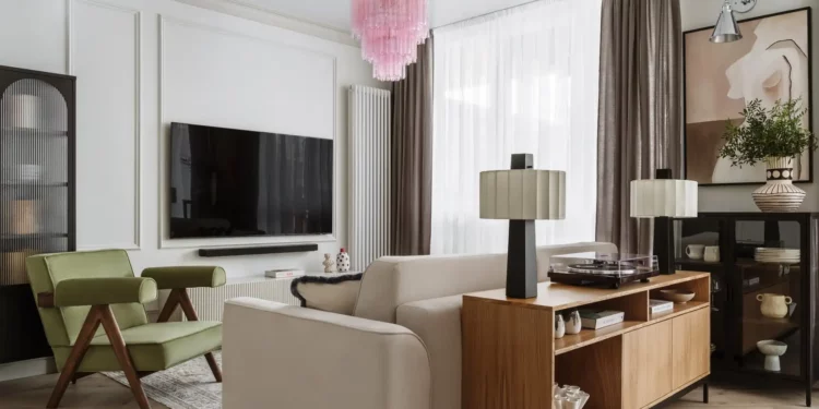 Nappali bézs kanapéval, zöld fotellel, falra szerelt tévével, fa konzollal és rózsaszín csillárral