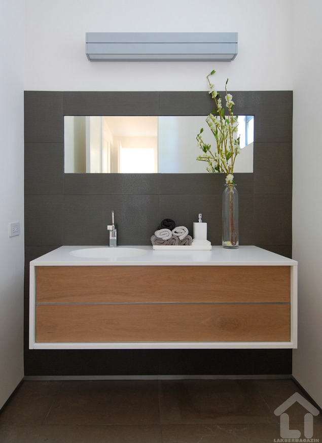 Fehér akril mosdó foglalja keretbe a fa frontú bútort, a nem mennyezetig érő falburkolat pedig az egész kompozíciót