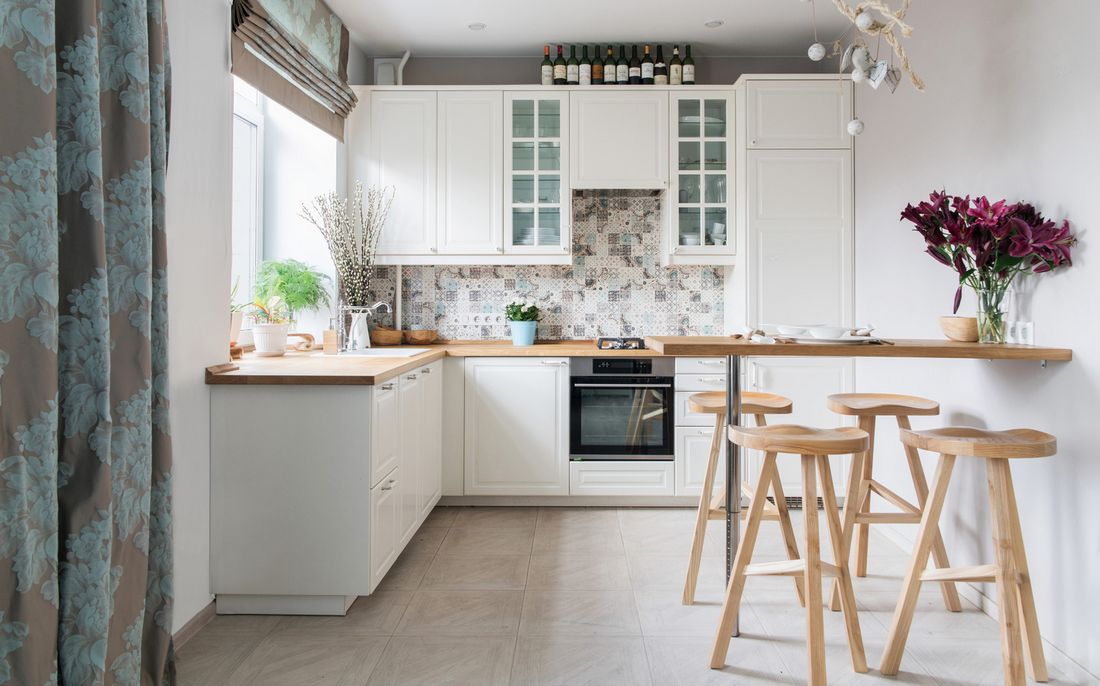 Világos konyha fehér bútorral, fa munkalappal és külön étkező 4 bárszékkel