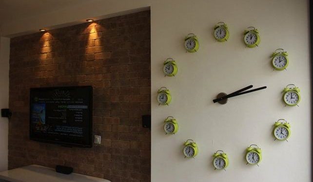 egy ötletes és hatalmas óra a falon, melynek számait az adott órára beállított öreg vekkerek adják